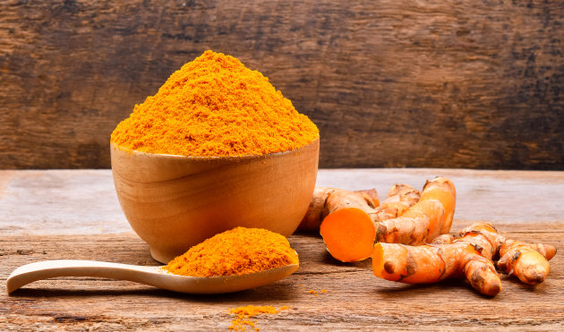 Turmeric roots with turmeric powder on wooden background