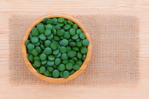 green pills spirulina and chlorella seaweed close up in a wooden bowl top view with frame